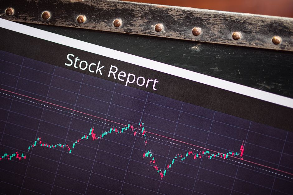 Close-up image of a computer screen displaying a stock report with a line graph illustrating fluctuating market trends, situated inside a property with a wooden and metal frame at the top. Behind the screen, a variety of packing materials, cardboard boxes, and furniture are visible, including a wardrobe and a table, indicating a house clearance or home relocation process. The scene captures the interior environment of a residential property during a furniture transport or packing and moving activity managed by Man with Van Ruxley, with natural lighting illuminating the space. The chart's data emphasizes the importance of logistical planning and accuracy in house removals, especially when dealing with business stock or other valuable items during a household move.